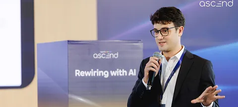 Cory speaking on stage at Agoda Ascend 2026, beside a “Rewiring with AI” sign